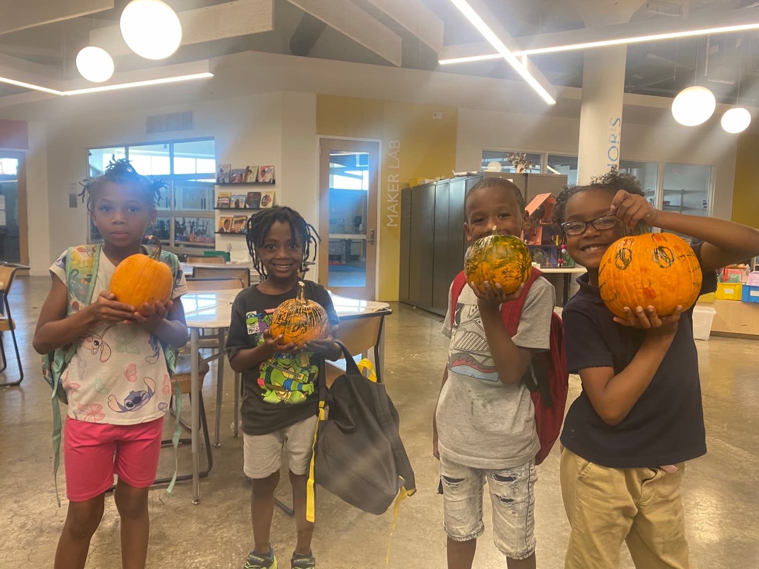 Four children proudly holding their decorated pumpkins during a creative program activity